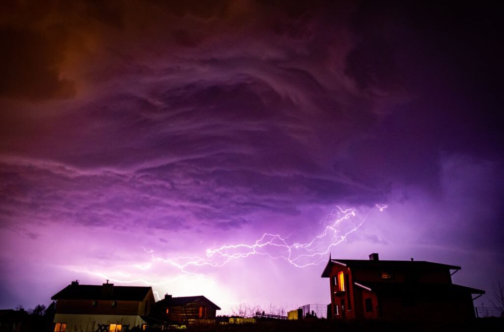 Several houses under a purple-hued cloudy sky with lightning.